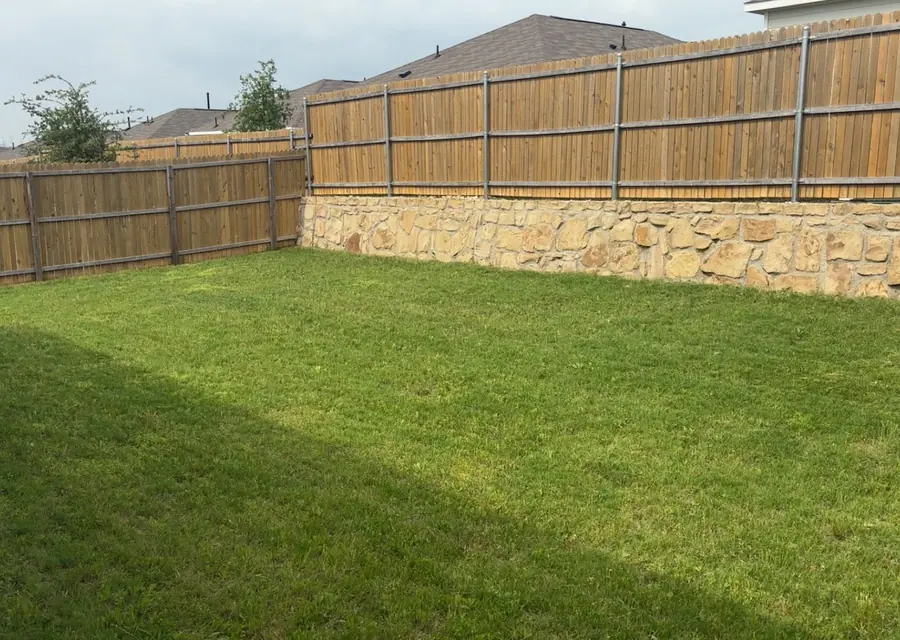 Back lawn mowed to an even finish along a timber fence in Saginaw, TX